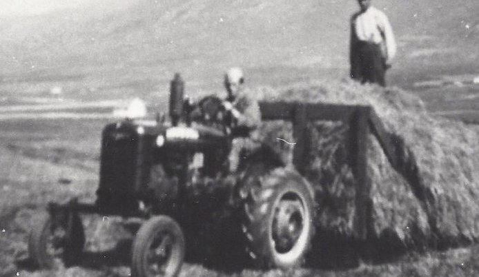 Hey flutt á fjórhjólavagni í Ytra-Garðshorni í Svarfaðardal. Hjalti Haraldsson (?) á dráttaravélinni og Haraldur Stefánsson (?) á heyinu. Myndin er tekin 1950 – 1960.